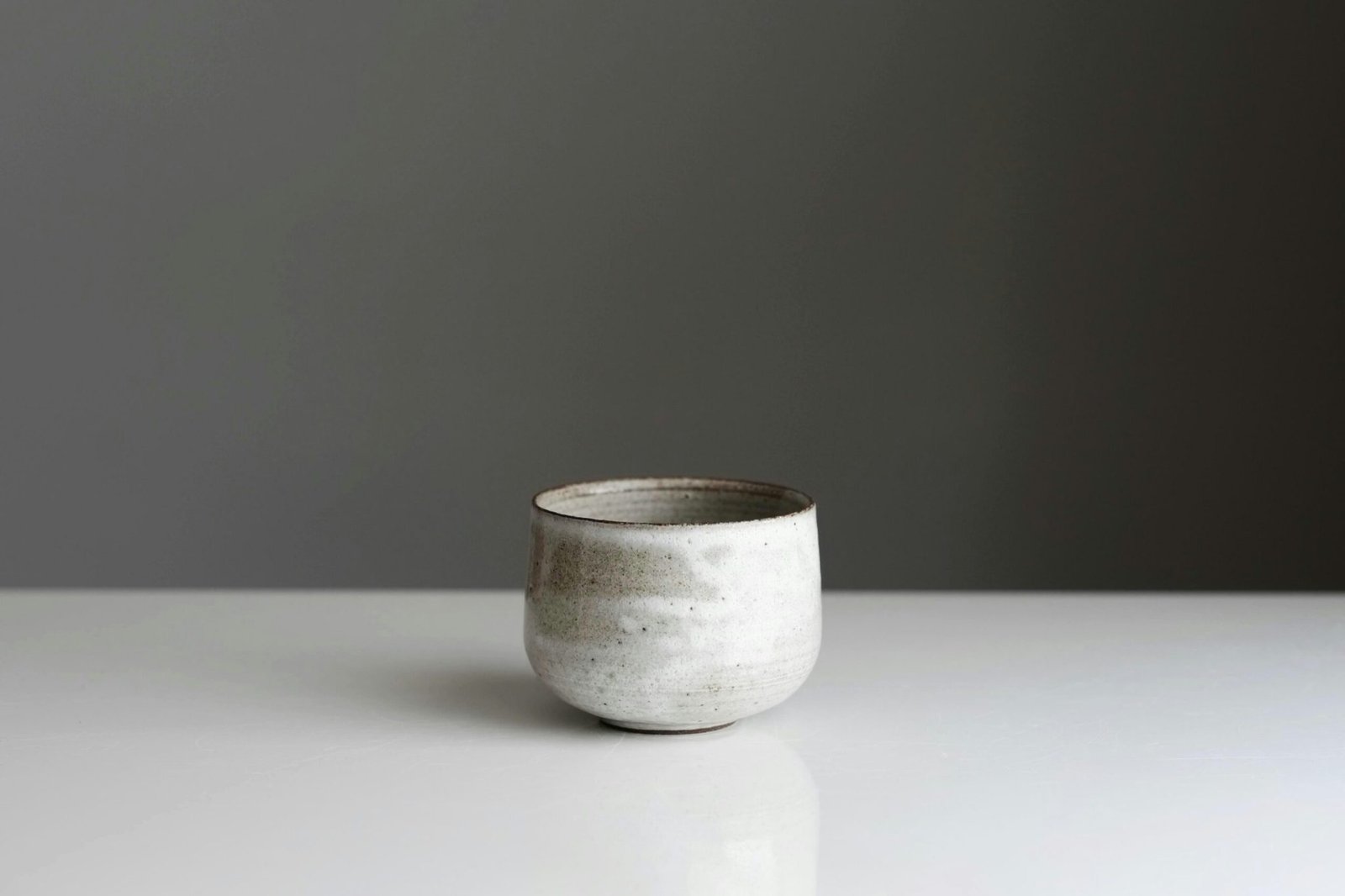 A white speckled ceramic chawan resting on a pale surface
